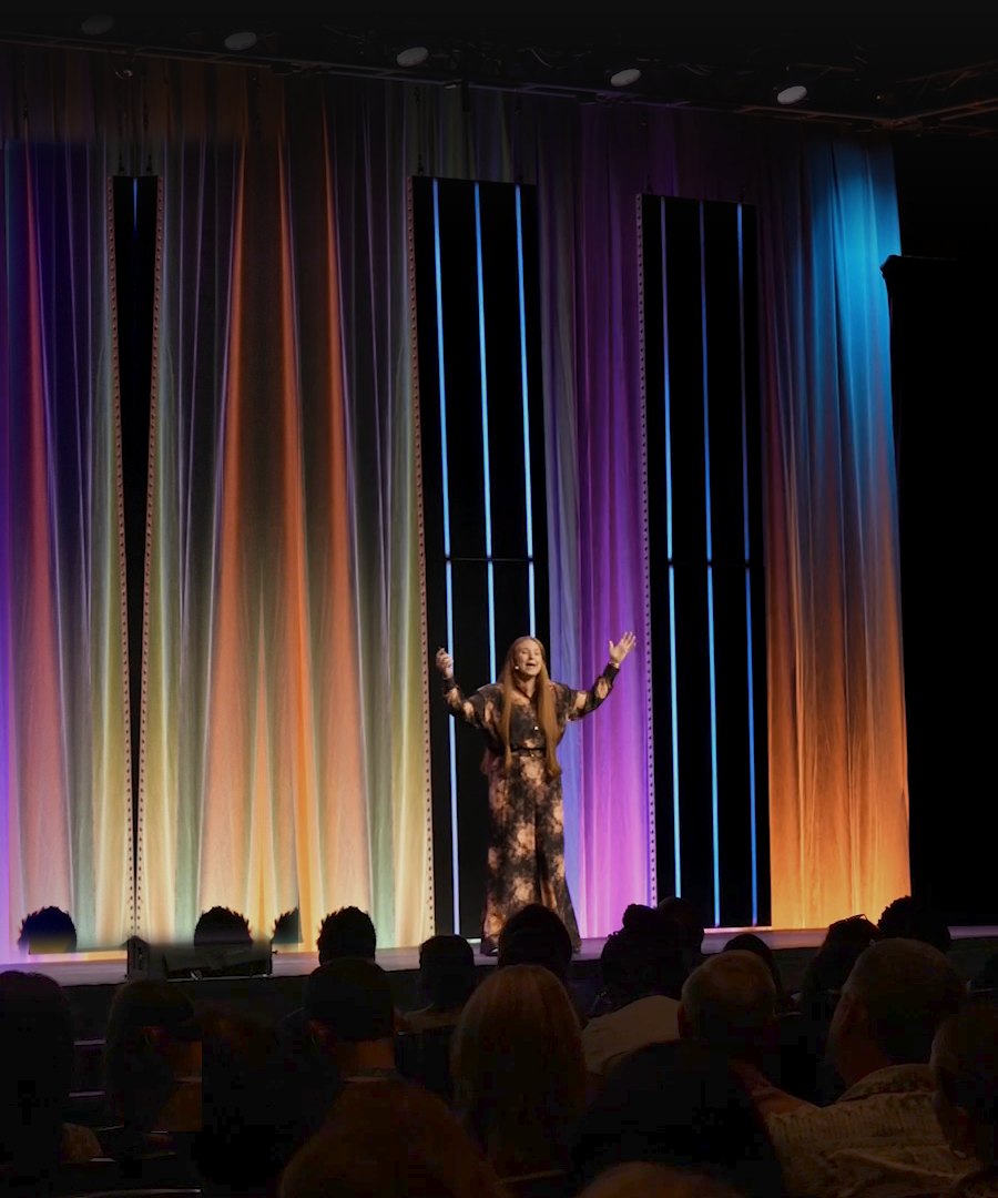 Kristina on stage at a keynote, arms open, speaking to a full room