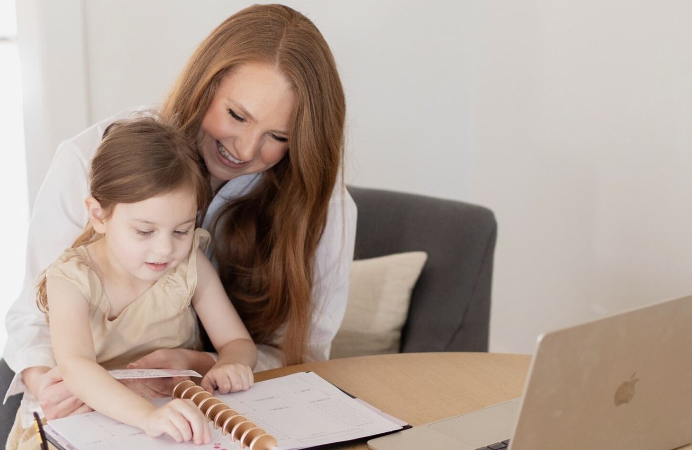 Kristina working at her laptop with her daughter beside her