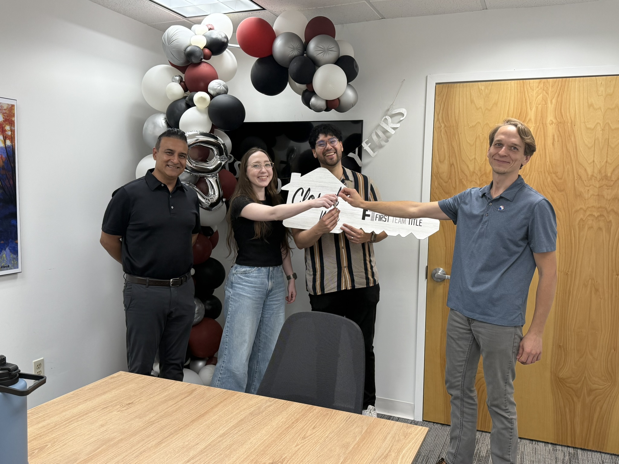 Four people celebrating with a large ceremonial key and balloons.
