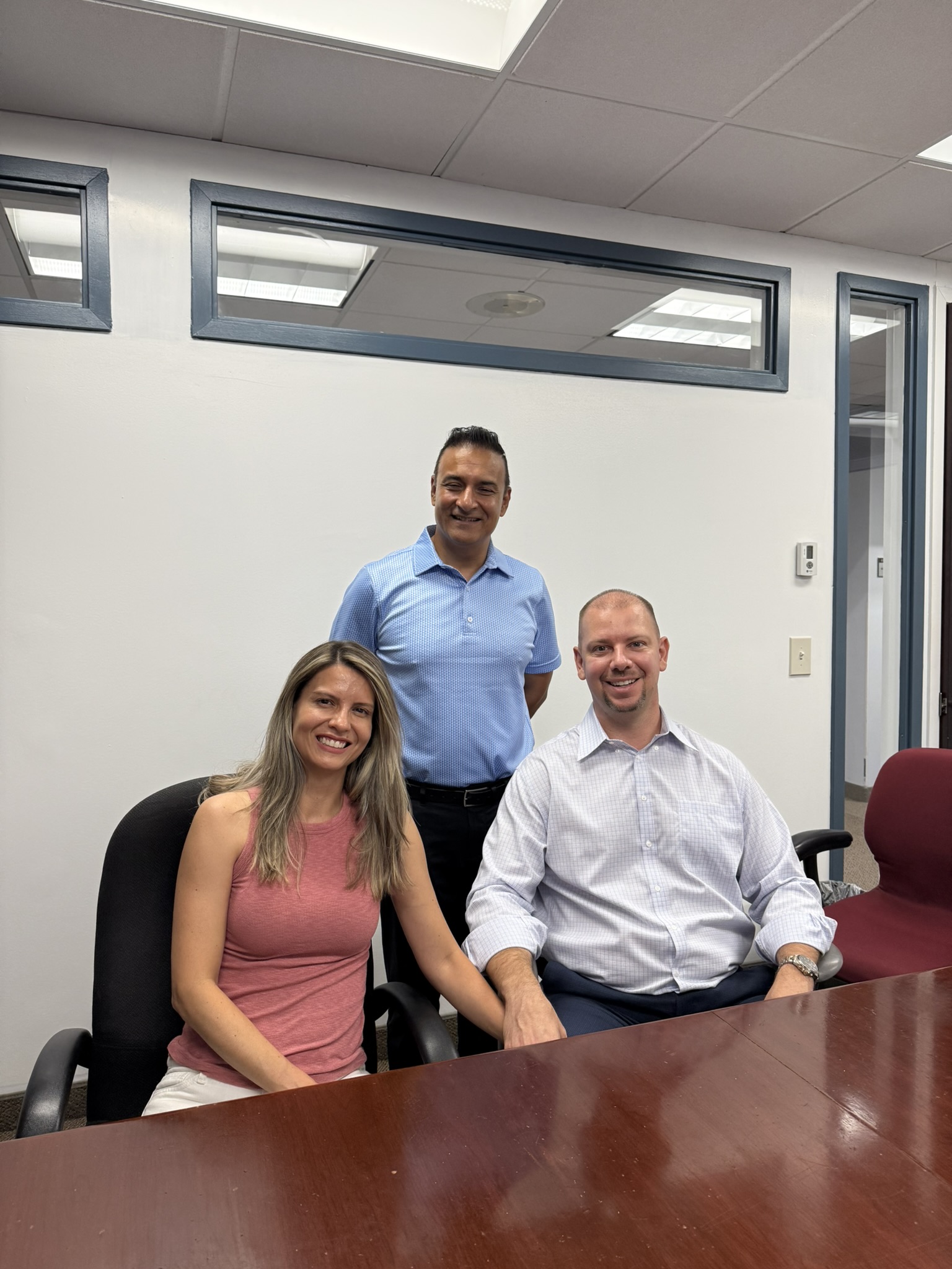 Three people smiling together in a meeting room.