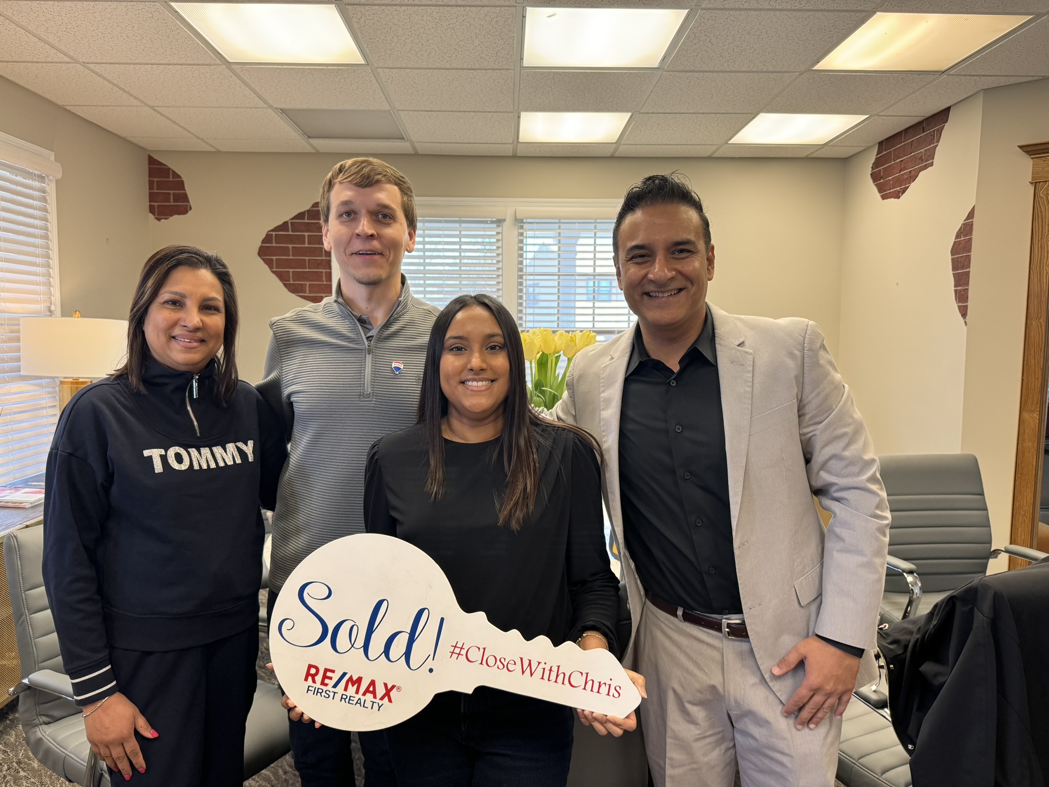 Four people standing together with a Sold sign at a closing celebration.