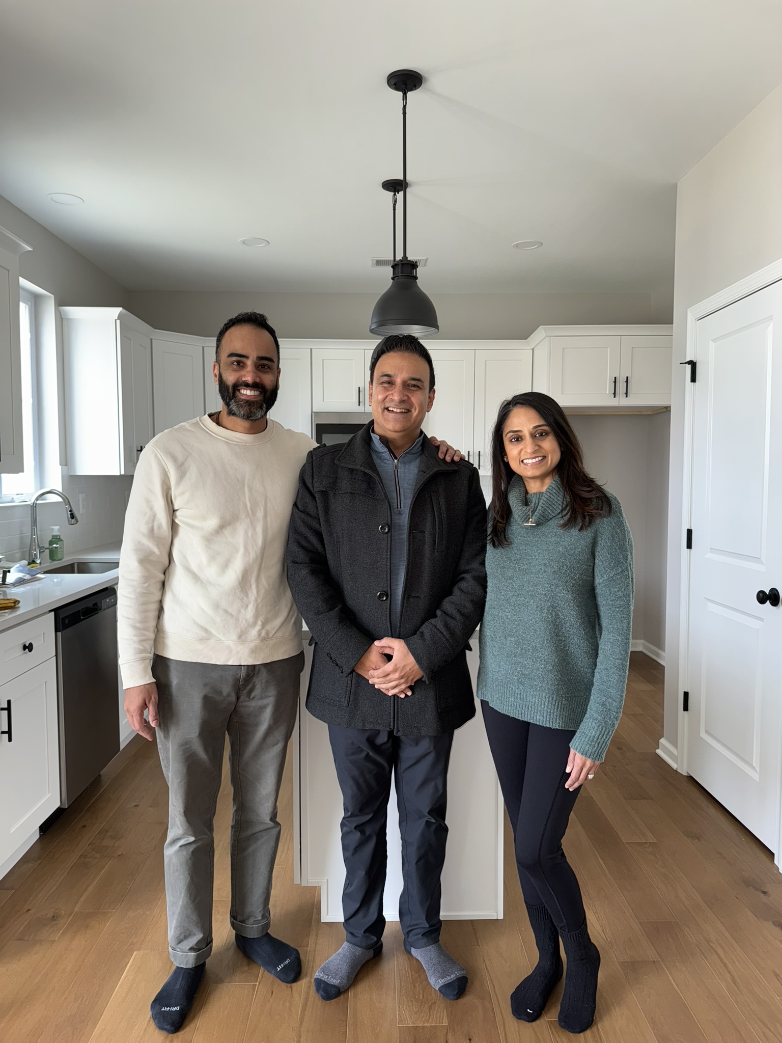 Three people smiling together in a bright home kitchen.