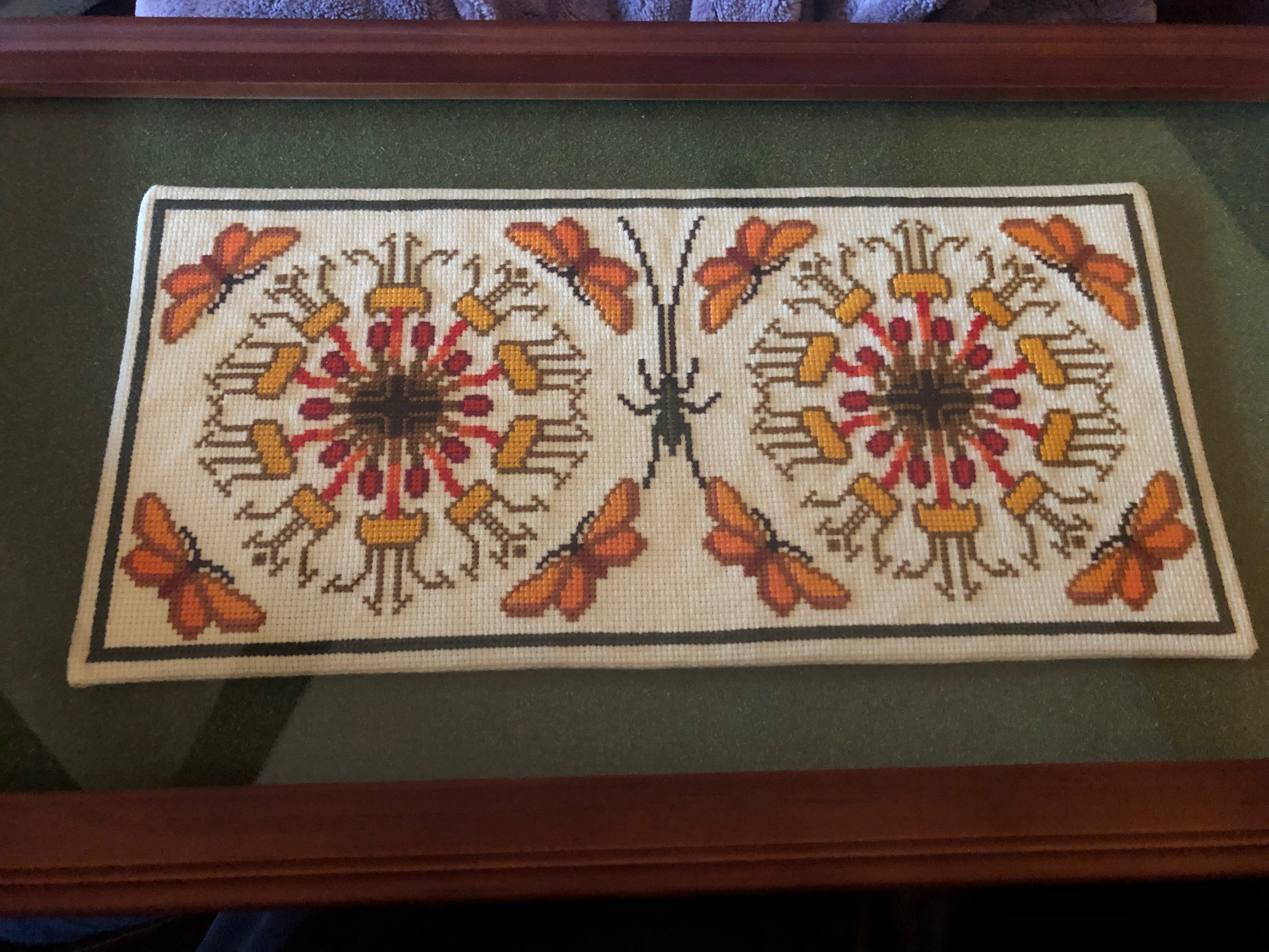 completed cross-stitch project of flowers surrounded by butterflies and a katydid