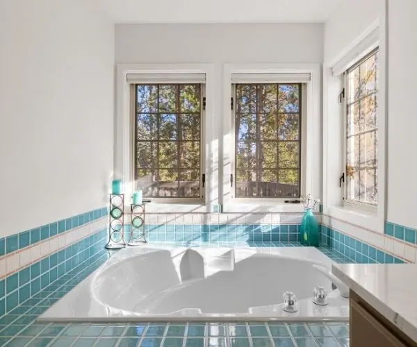 Luxury ADU bathroom design in Bend, OR, featuring a large freestanding soaking tub, turquoise accent tile, and three large windows for natural light. Modern spa-style guest house renovation.