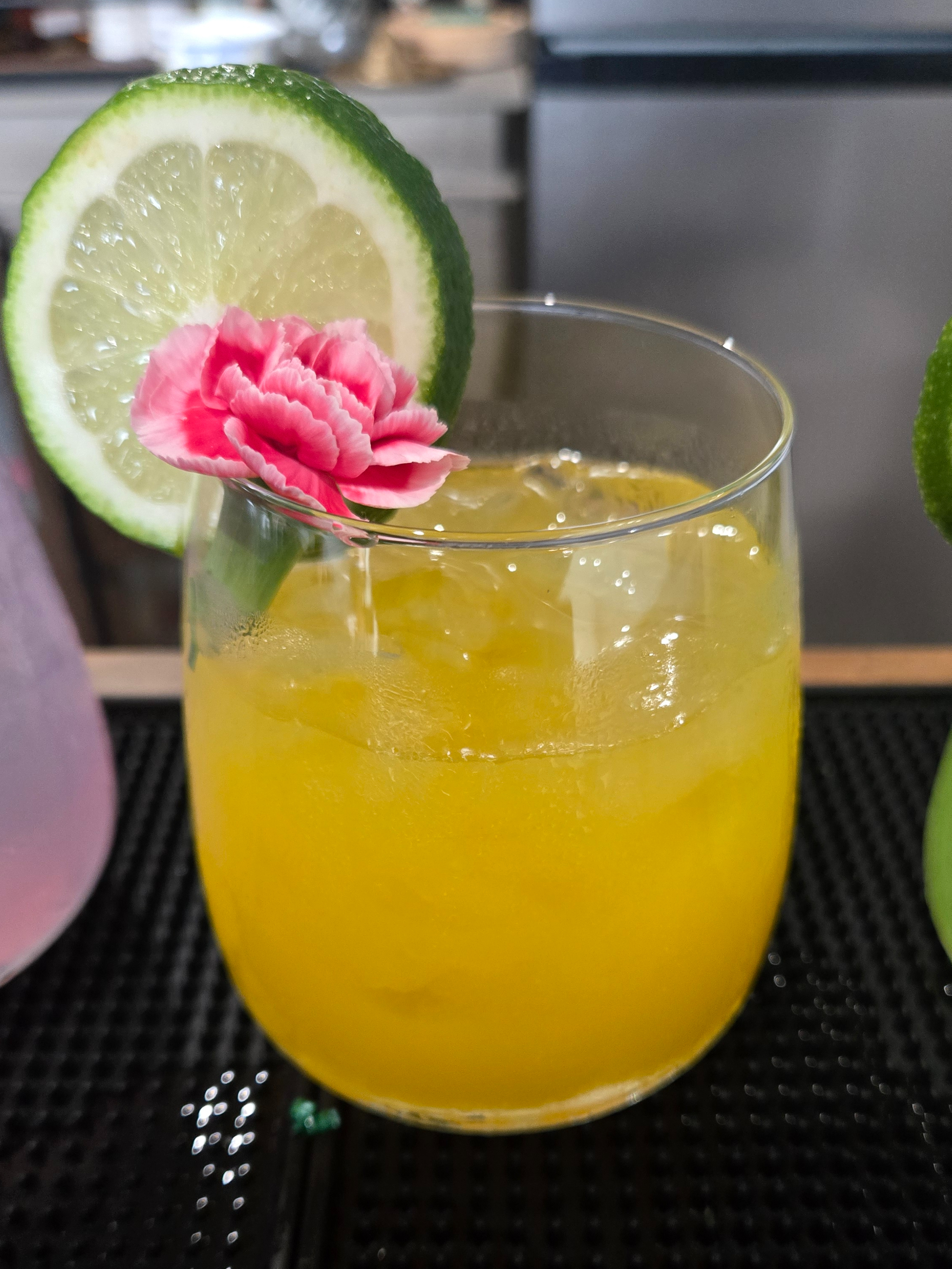 Yellow cocktail garnished with a flower and lime