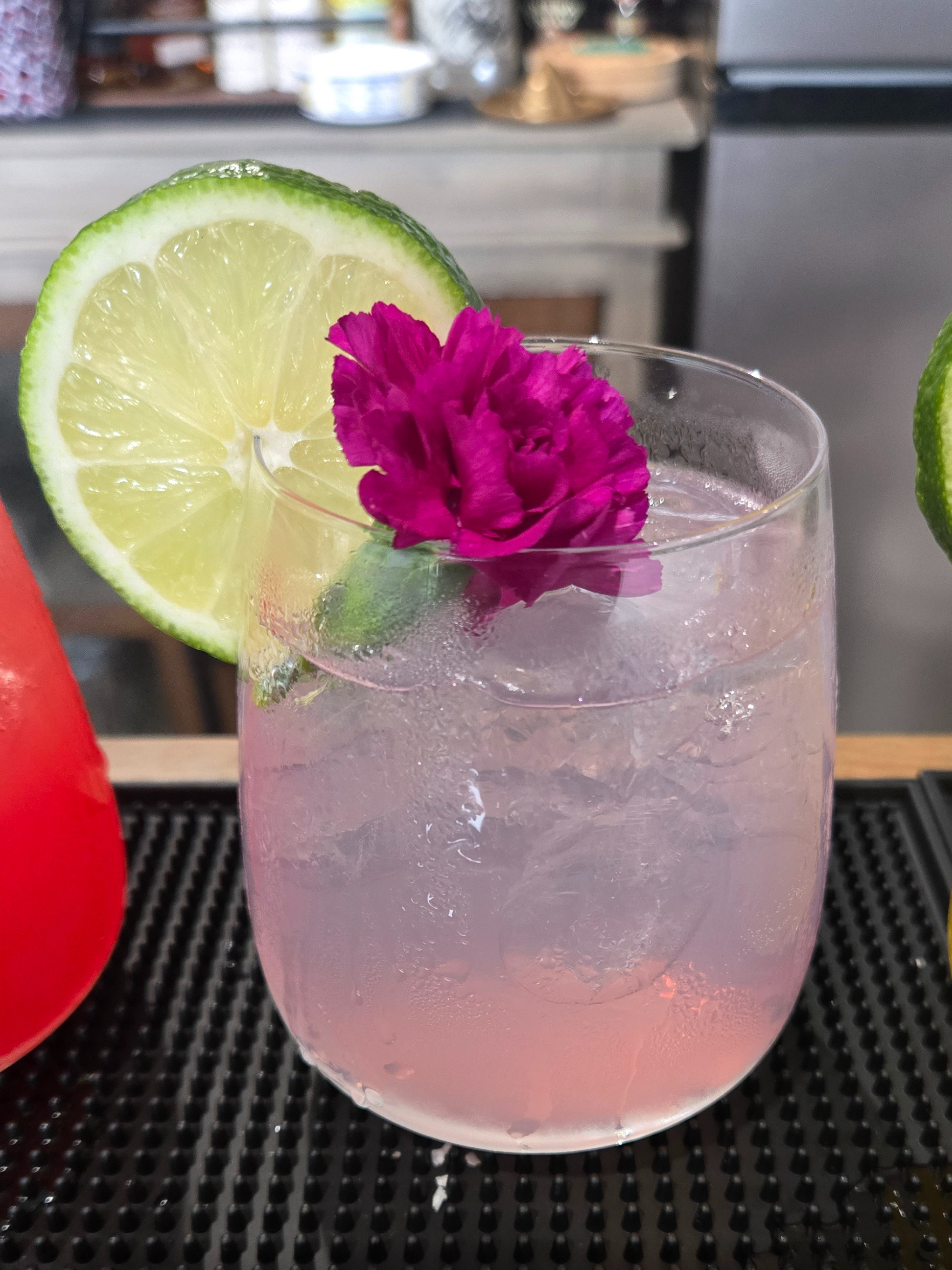 Pink cocktail garnished with a lime wheel and magenta flower on a bar mat