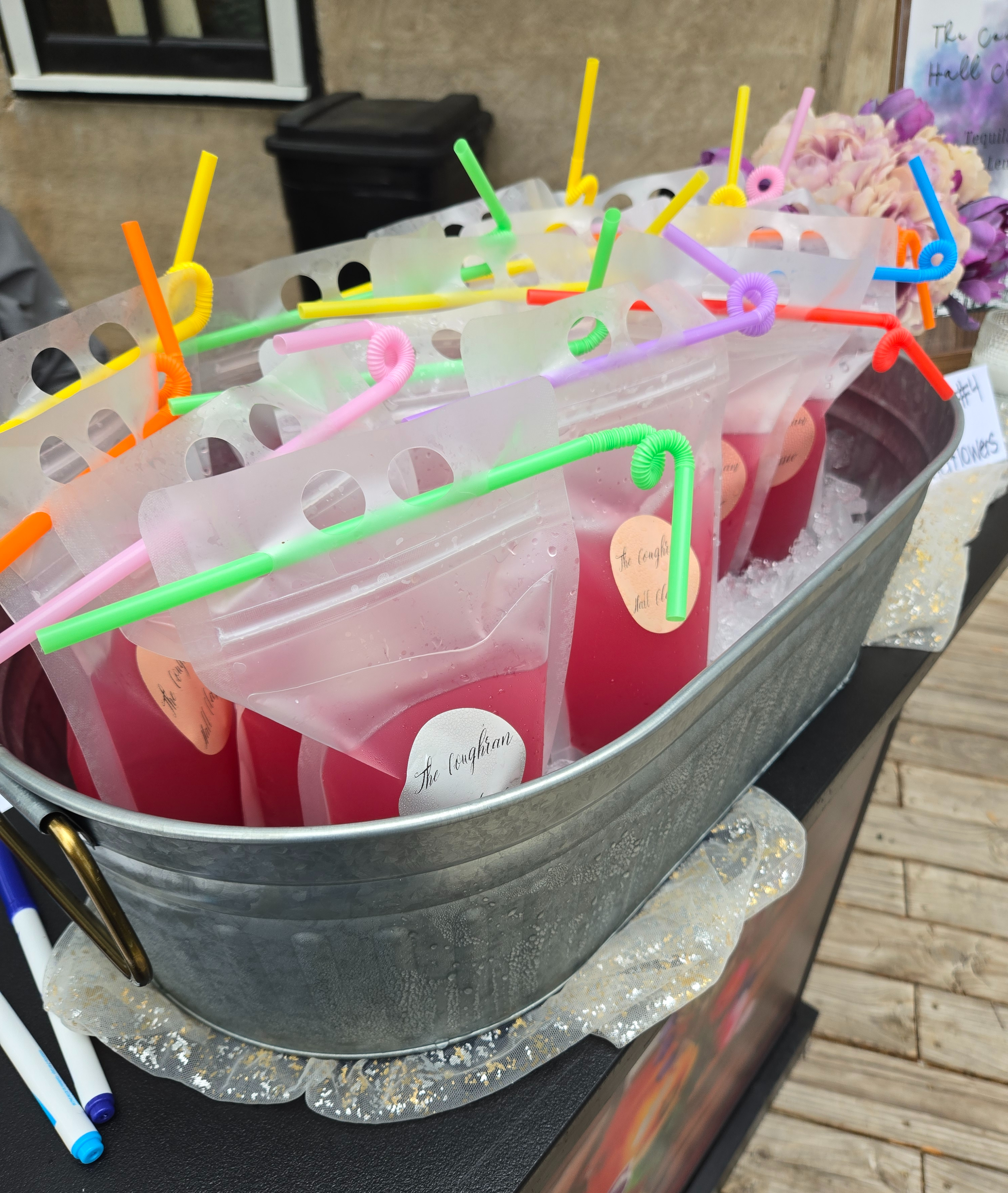 Pre-batched cocktail pouches with colorful straws chilling in an ice-filled metal tub