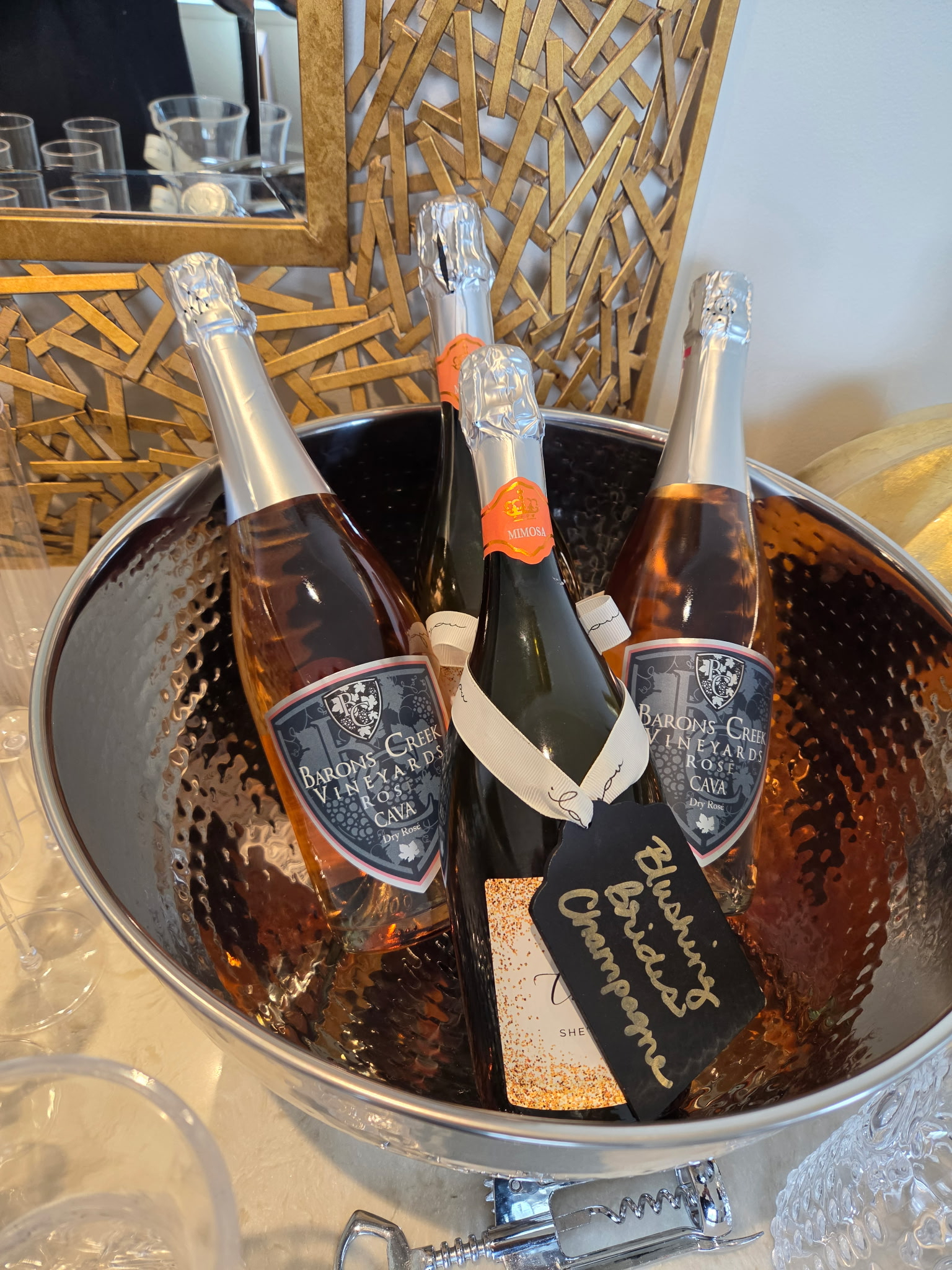 Bottles of sparkling wine chilling in an ice bucket with a chalkboard label at an indoor event