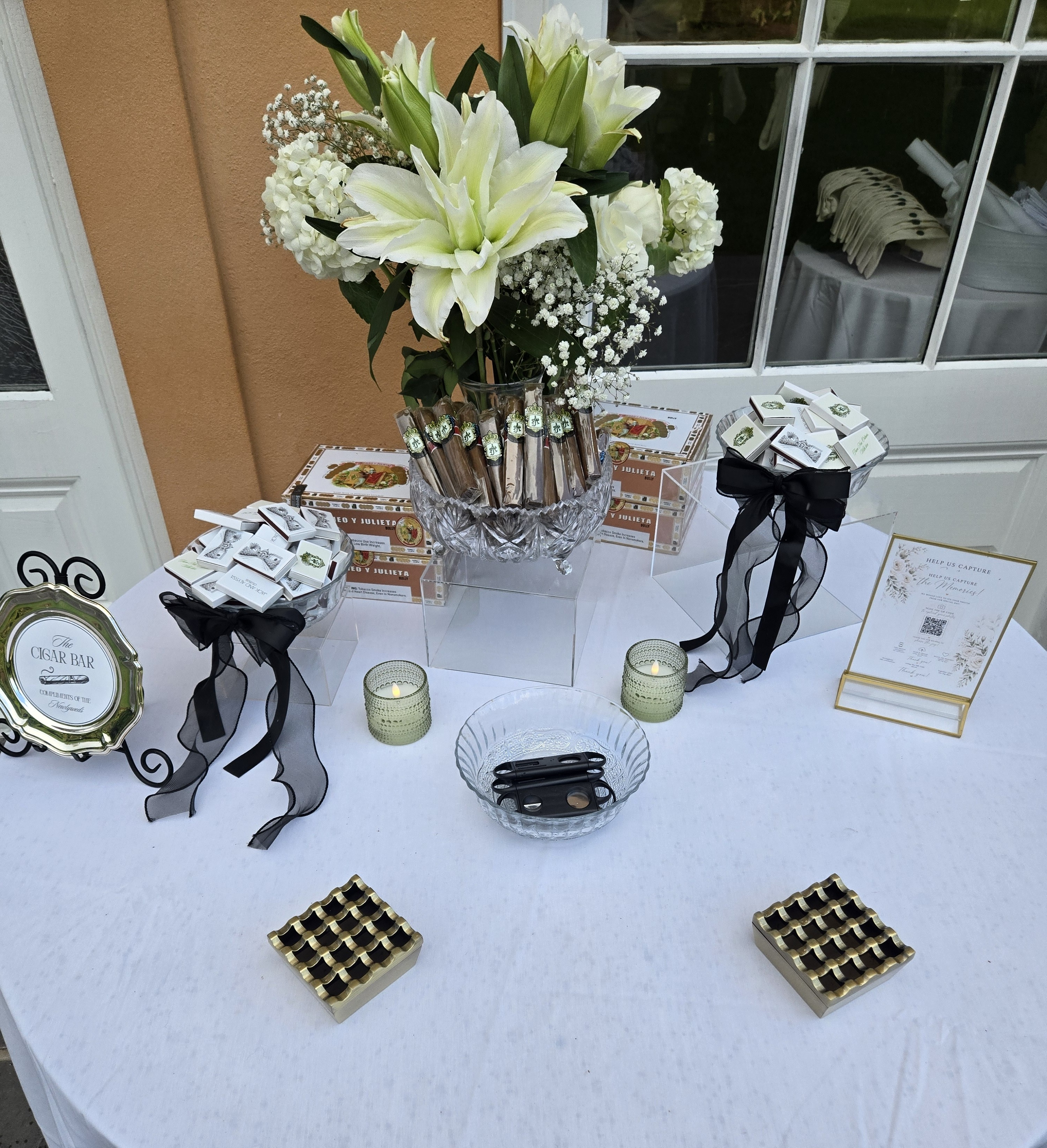 Styled cocktail table with cigar favor boxes and florals in black, white, and gold
