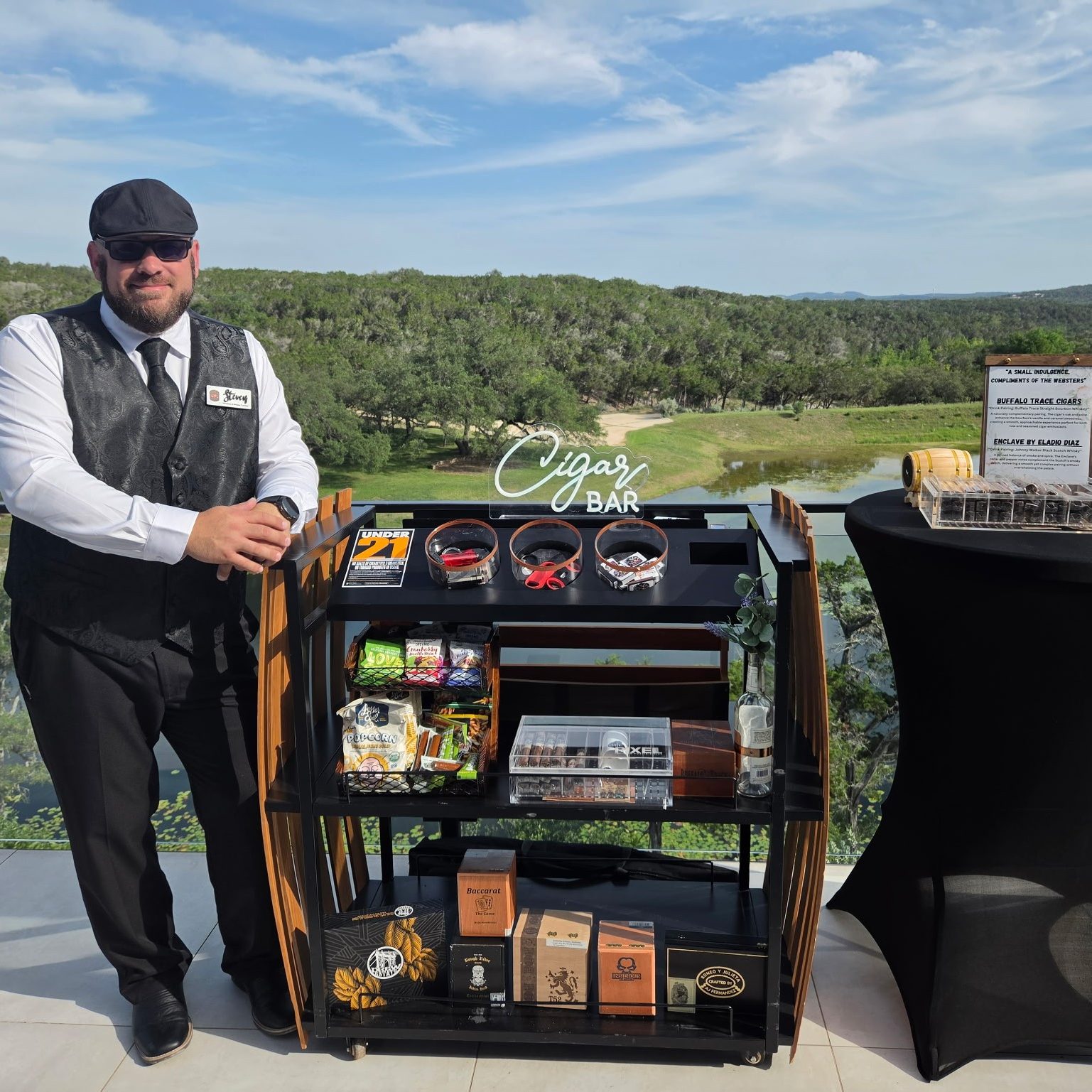 Cigar Bar attendant beside illuminated cart with whiskey pairing menu overlooking a Hill Country lake