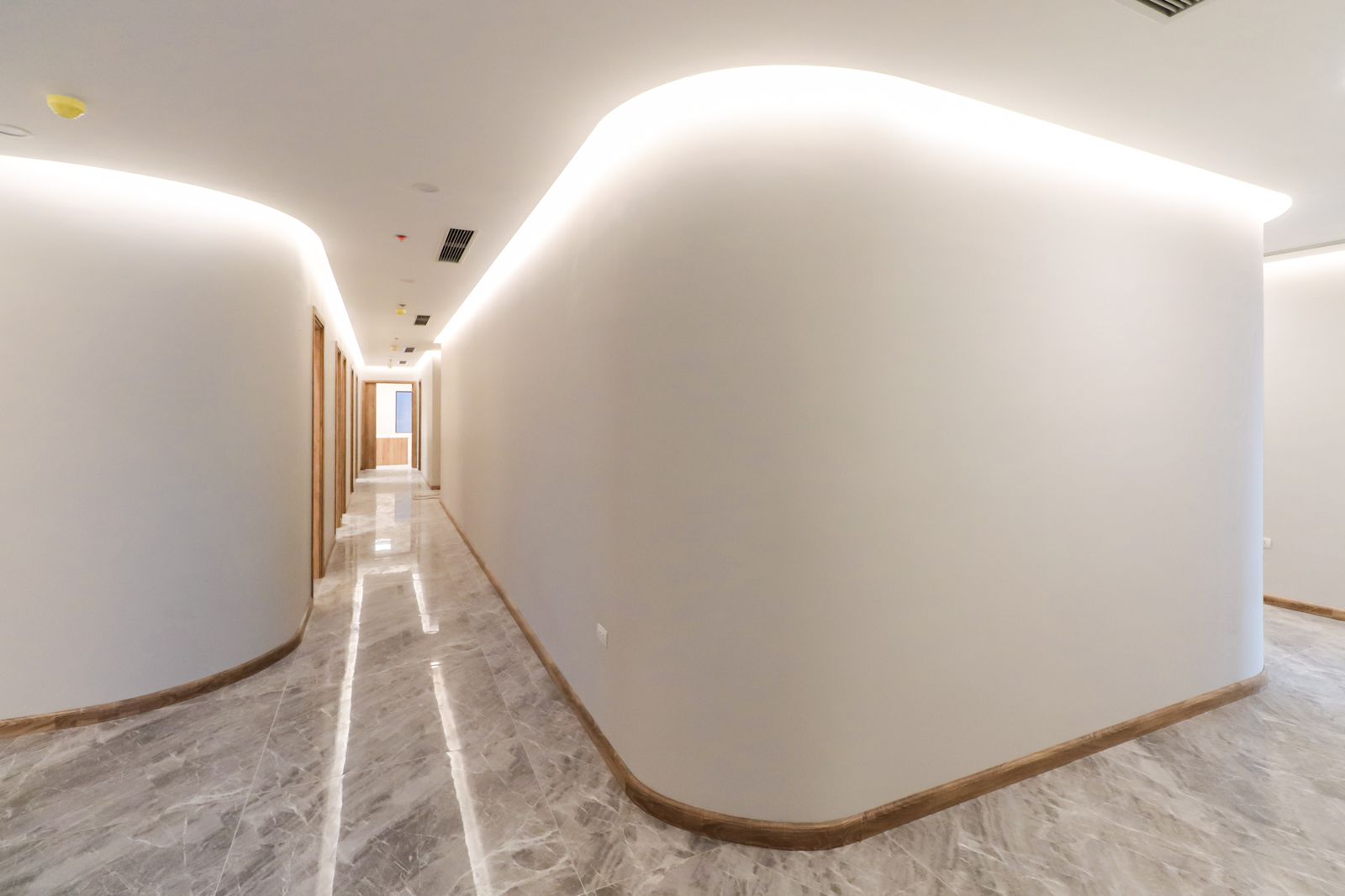Bright modern hallway with curved walls, soft lighting and a marble floor