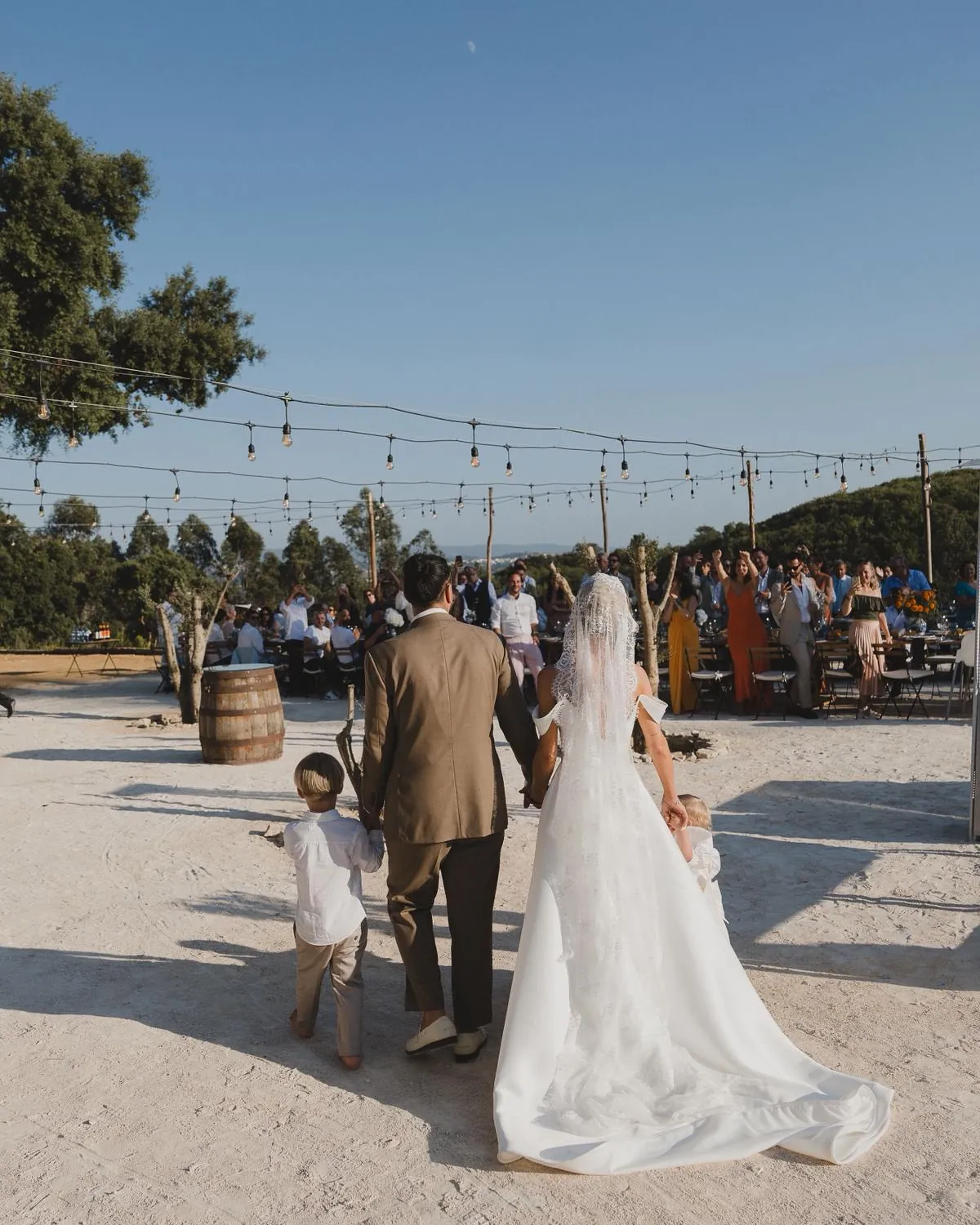 Brautpaar geht mit Kindern unter Lichterketten zum Fest in Portugal