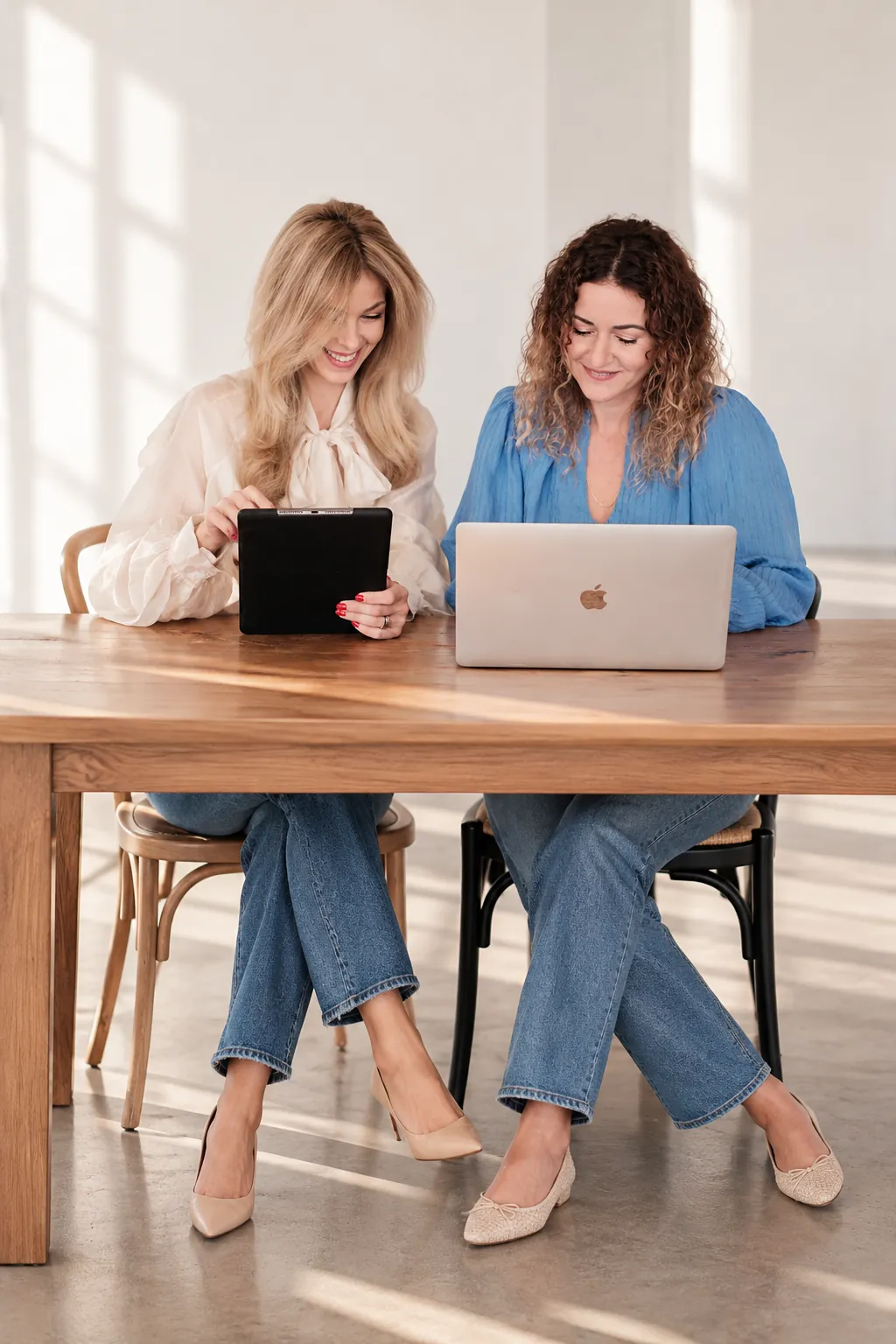 Andrea und Kim planen am Tisch mit Tablet und Laptop eine Hochzeit