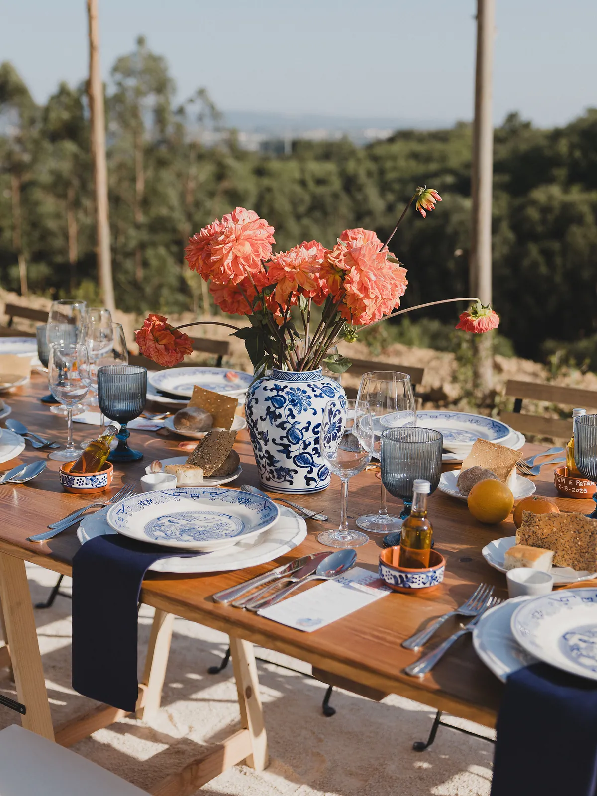 Hochzeitstafel mit orangen Blumen in einer blau-weissen Vase und blauem Geschirr