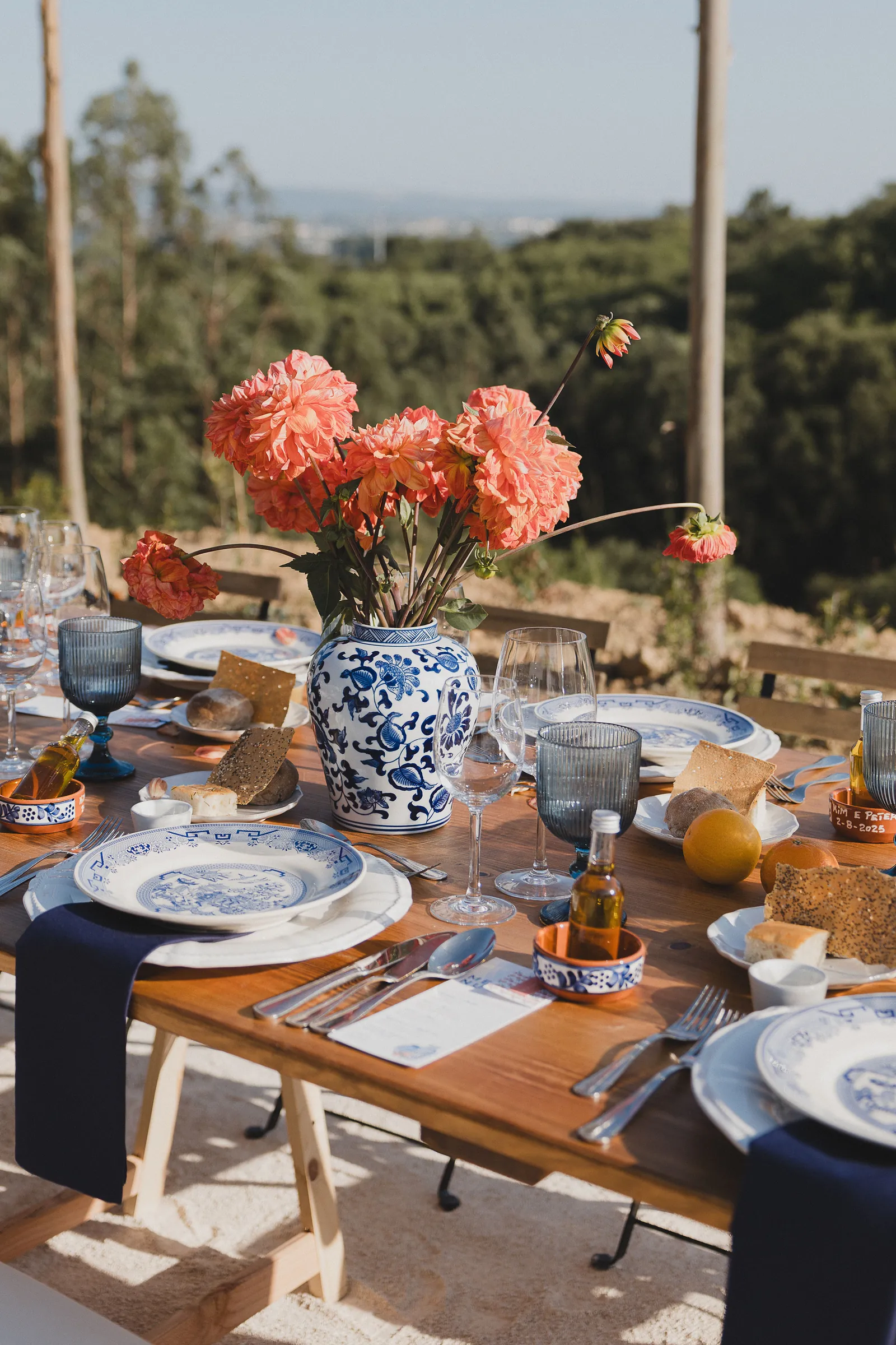Hochzeitstafel mit orangen Blumen in einer blau-weissen Vase und blauem Geschirr