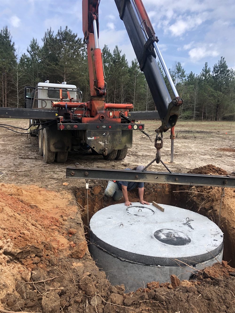 Holmes Septic boom truck lowering a precast concrete tank into an excavated hole