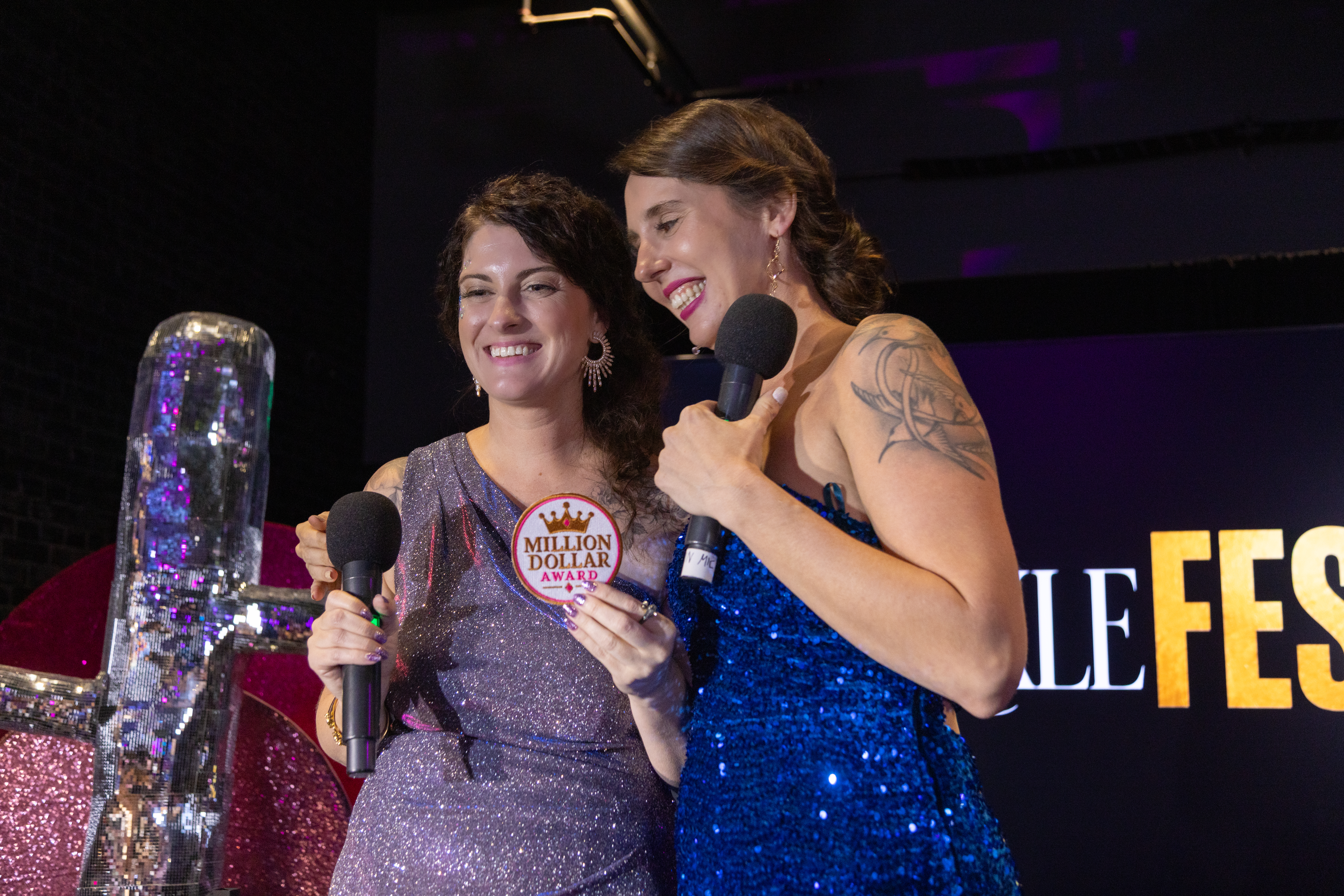 Two speakers sharing a celebratory moment with microphones on the SparkleFest stage.