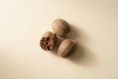 Džiovintas ingredientas ant kreminio fono: Muskato riešutas.