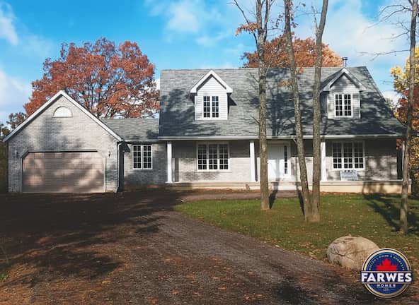 Grey brick Farwes custom home with dormers and a side garage among autumn trees