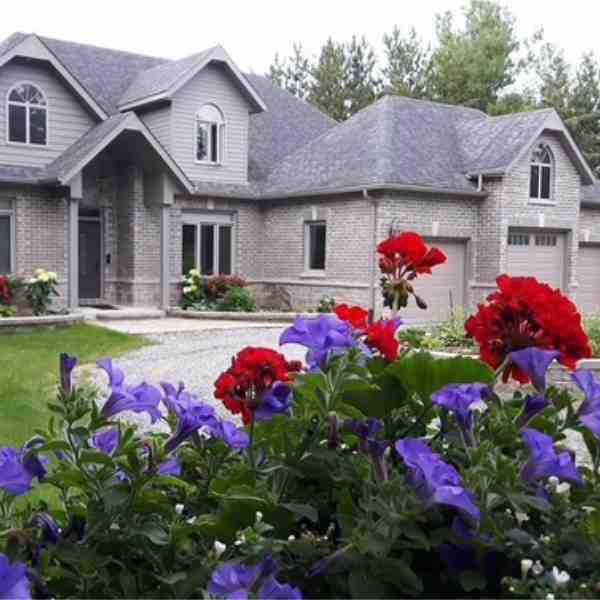 Grey brick Farwes custom home with gardens and a gravel drive