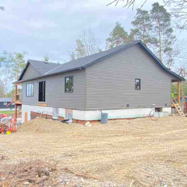 Grey siding Farwes house under construction on a treed lot