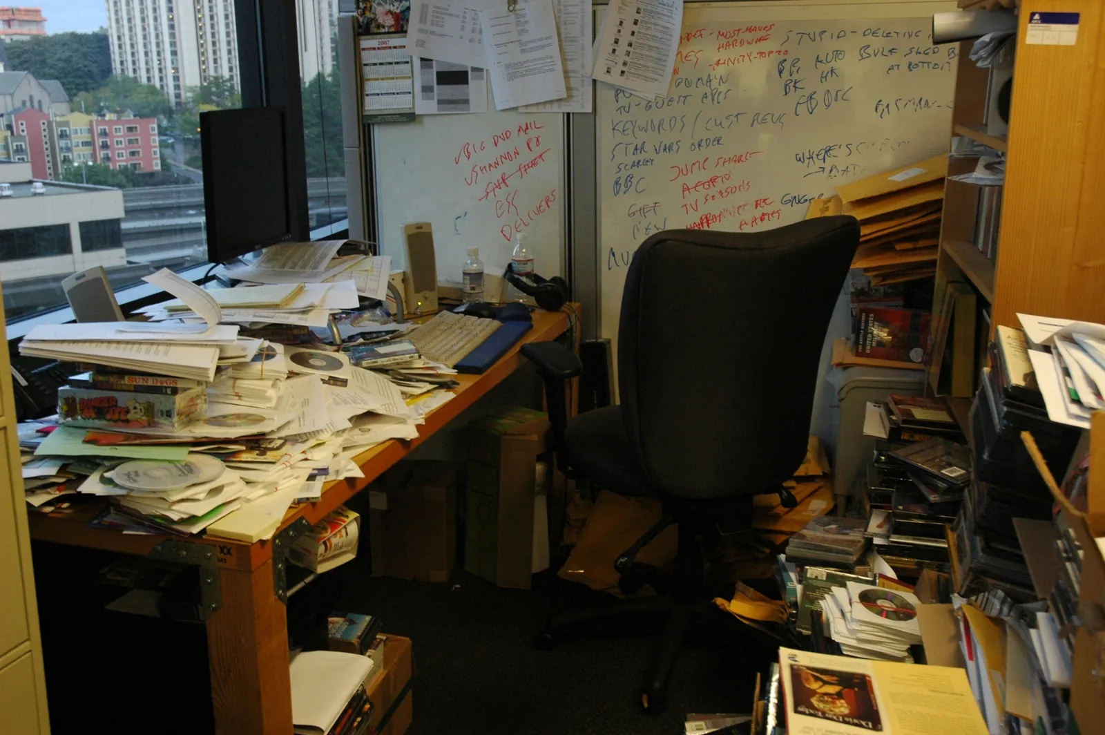 Cluttered office desk piled high with papers and binders