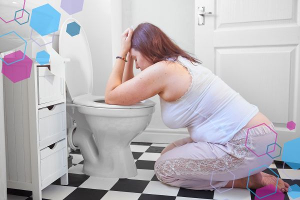Pregnant person kneeling by a toilet experiencing nausea and vomiting in early pregnancy.