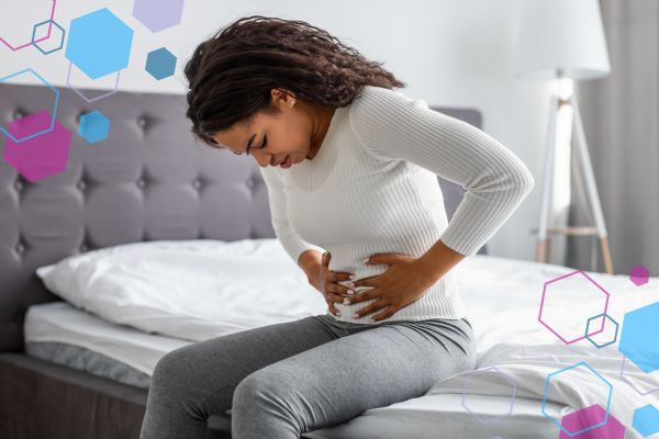 Person sitting on a bed holding their lower abdomen, illustrating cramping and abdominal discomfort in early pregnancy.