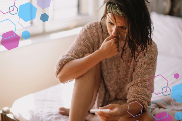 Person sitting on a bed holding a pregnancy test and looking concerned, reflecting uncertainty during early pregnancy symptoms such as spotting or discharge.