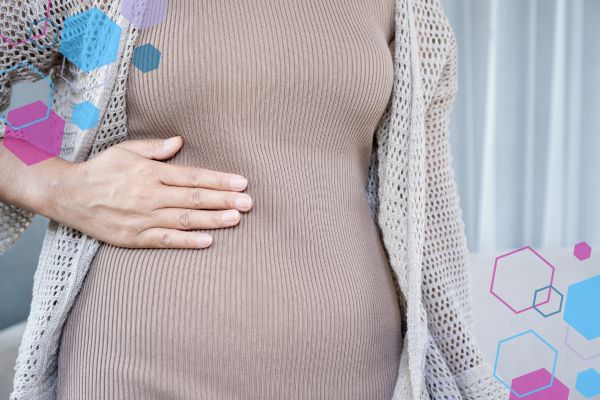 Close-up of a pregnant abdomen with a hand resting on one side, representing mild abdominal discomfort in early pregnancy.