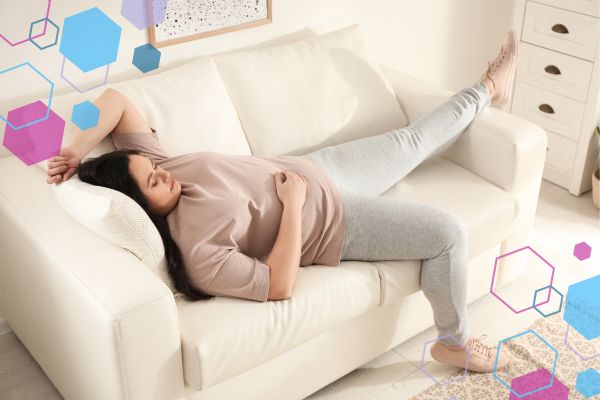 Person lying on a sofa with one hand on their abdomen, illustrating fatigue and physical heaviness in early pregnancy.