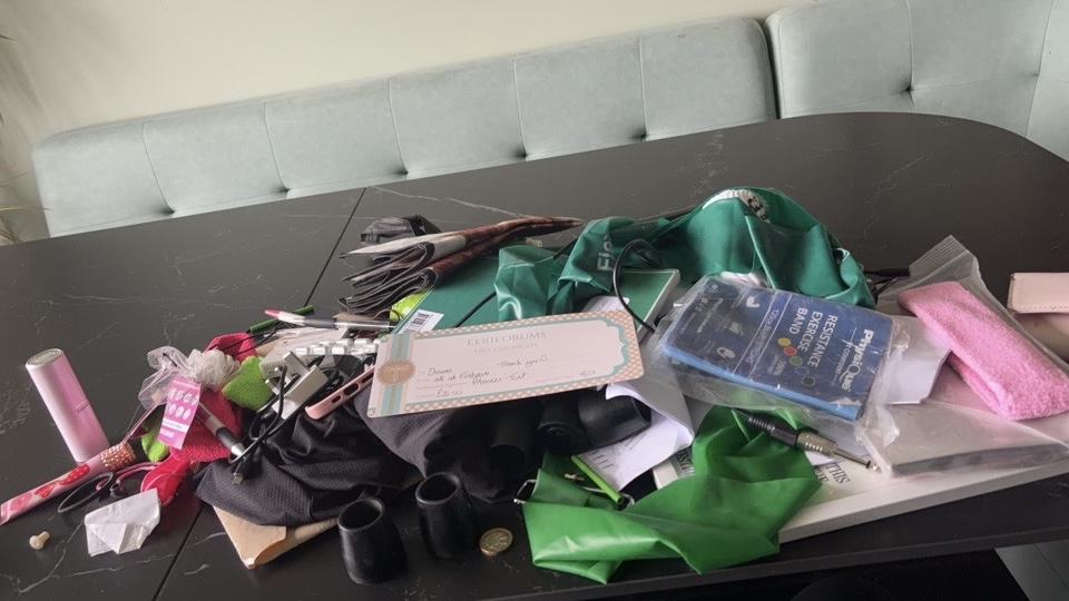 Resistance bands, cables, pens and paperwork emptied from Donna’s work backpack onto a table Resistance bands, cables, pens and paperwork emptied from Donna’s work backpack onto a table