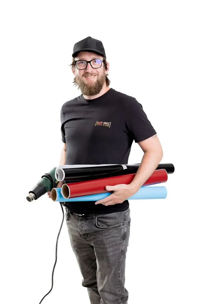 Andy Jones holding rolls of vinyl and a heat gun for vehicle graphics