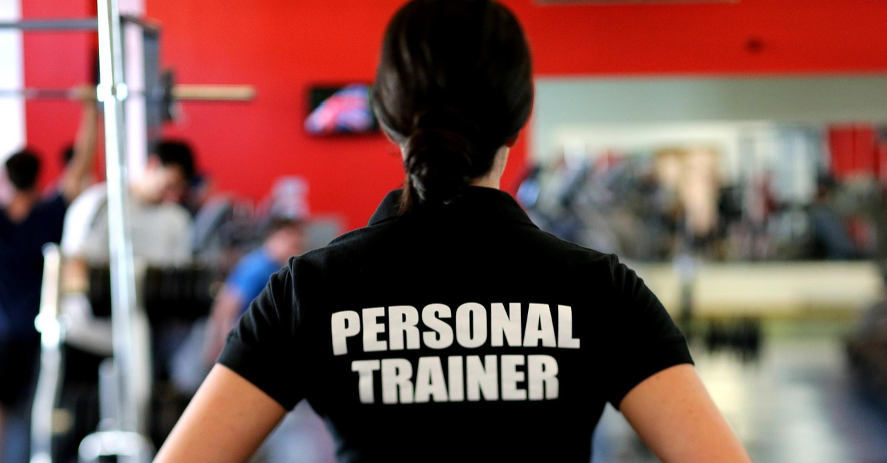 Personal trainer viewed from behind wearing a black Personal Trainer t-shirt in a gym