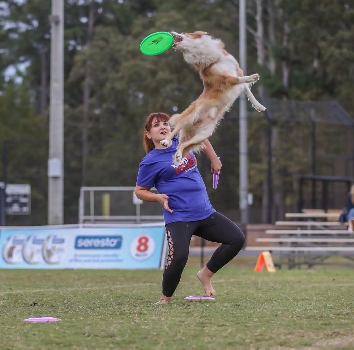 Andrea throwing a disc as her dog vaults overhead
