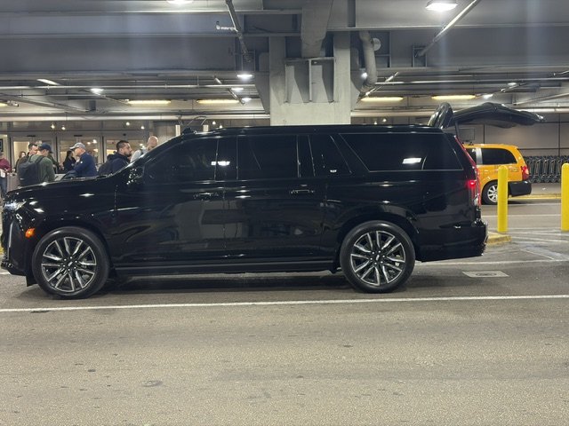 Black Cadillac Escalade ESV luxury SUV with liftgate open at an airport pickup zone — Opulent Transport fleet serving Fort Lauderdale and Miami airports