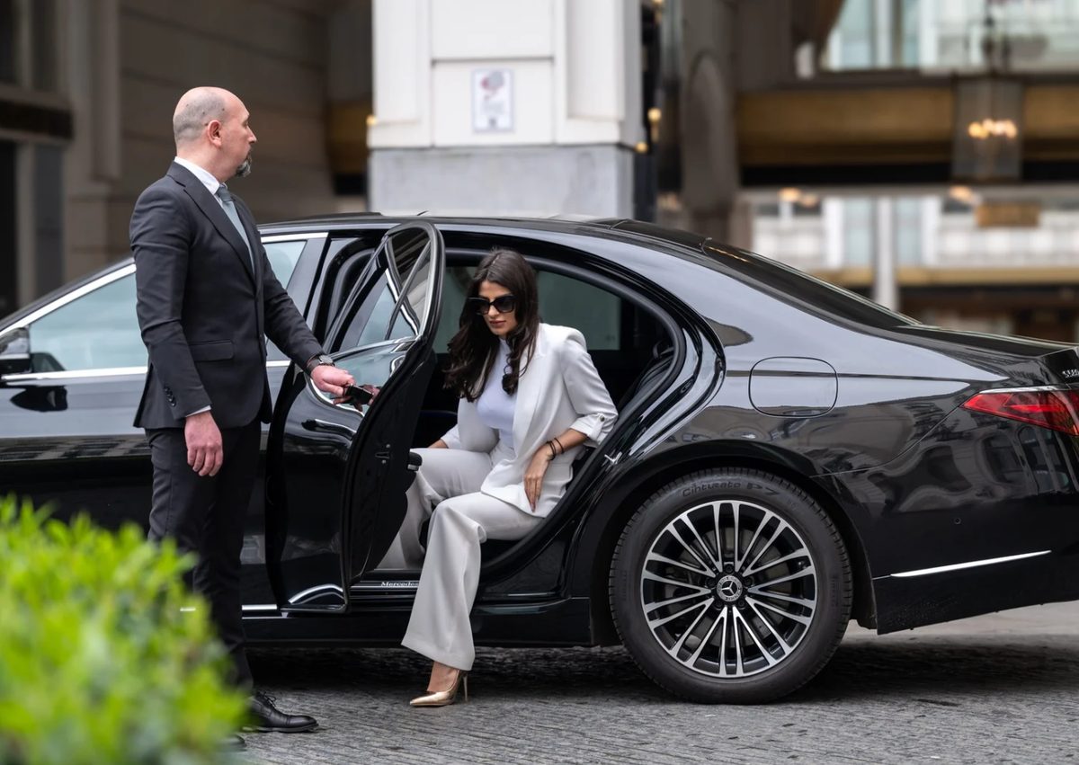 Professional chauffeur in dark suit opening the rear door of a black Mercedes-Benz S-Class for a client