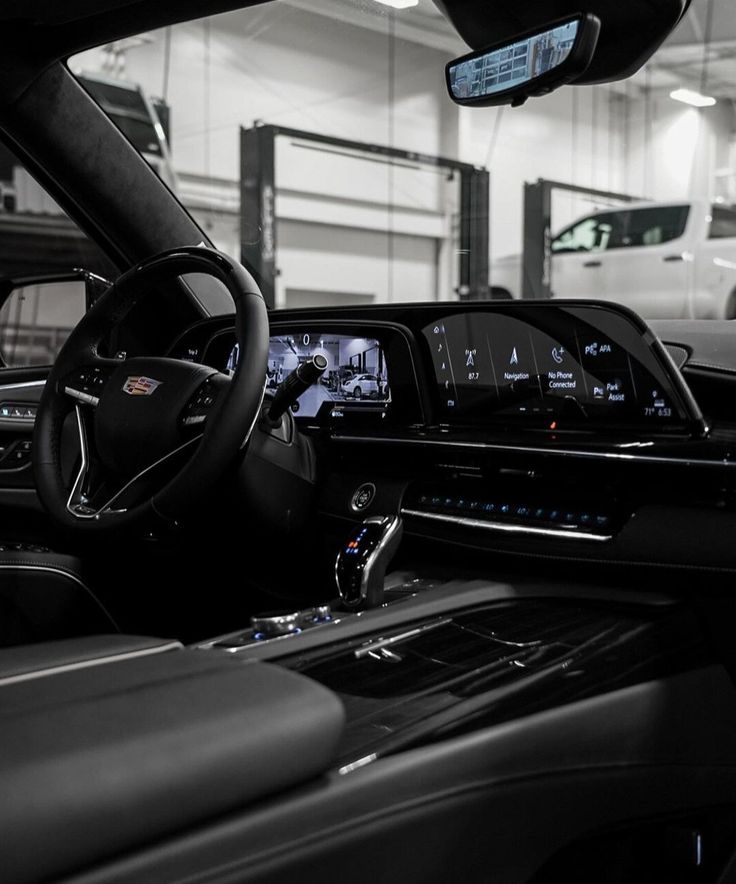 Driver's seat, steering wheel and curved dashboard display inside a black Cadillac Escalade