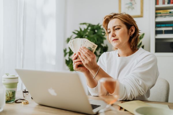 Woman sitting in front of a laptop holding cash, representing selling a house for a fast cash offer.”