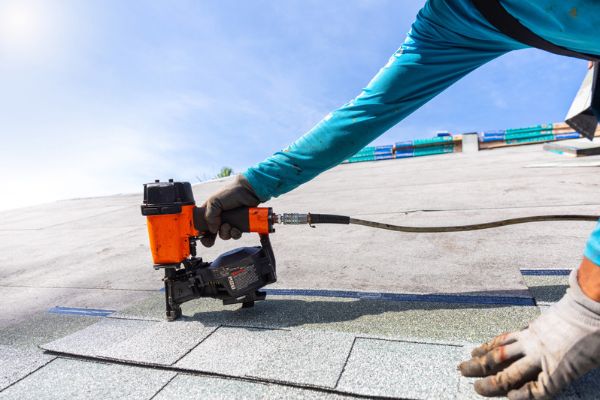 A worker installing shingles and securing exterior panels to ensure the structure is winter ready. A worker installing shingles and securing exterior panels to ensure the structure is winter ready.