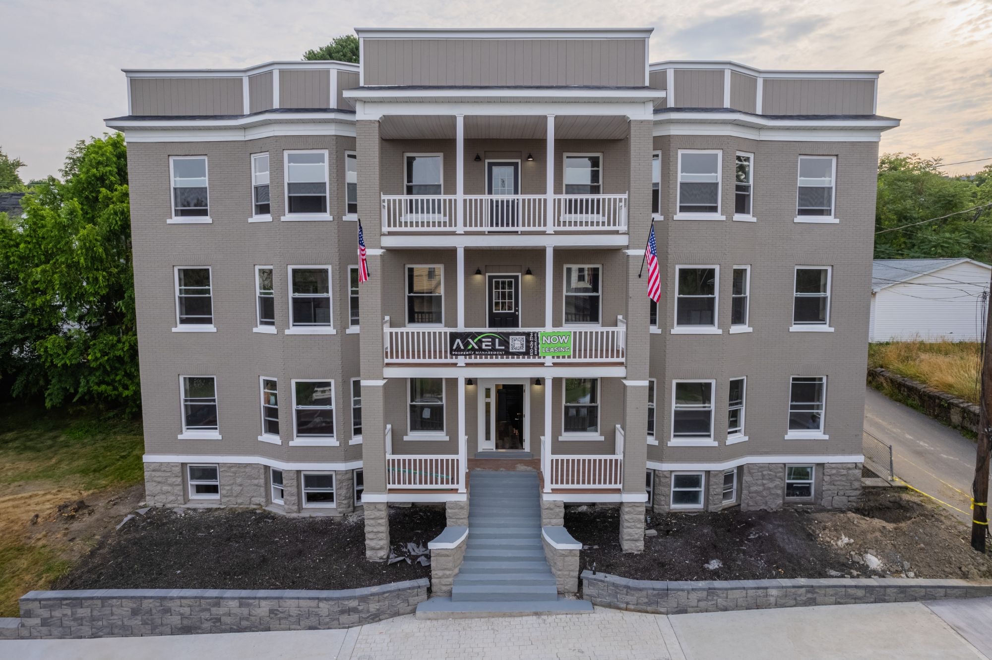The renovated 12-unit apartment building on Vine Street, Scranton: three storeys of grey brick with white trim, twin covered porches and a stone base, photographed at dusk.