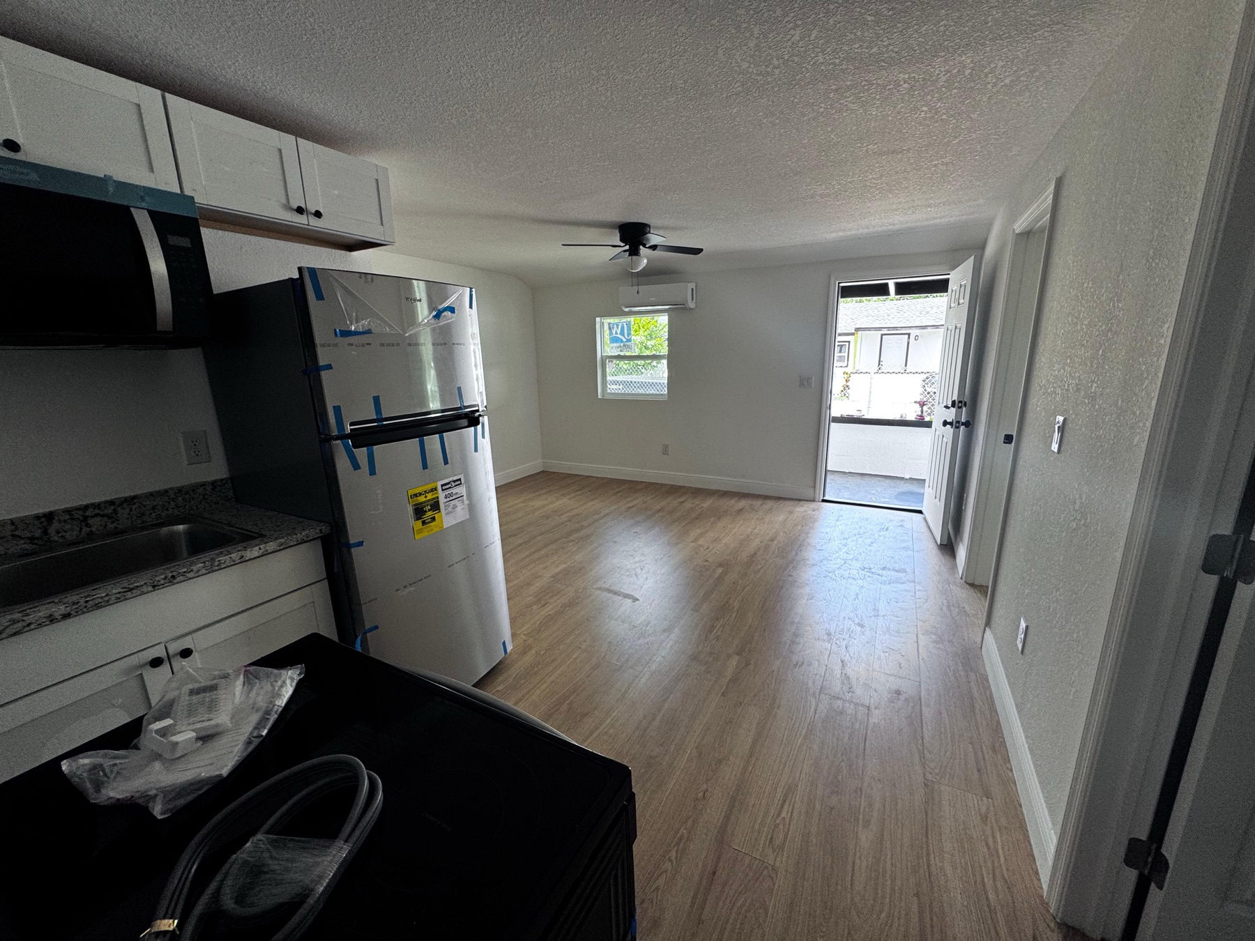 Inside a renovated unit at Tampa Heights: new wood-look flooring, fresh white walls, a wall-mounted air handler and a new refrigerator still in its protective film.