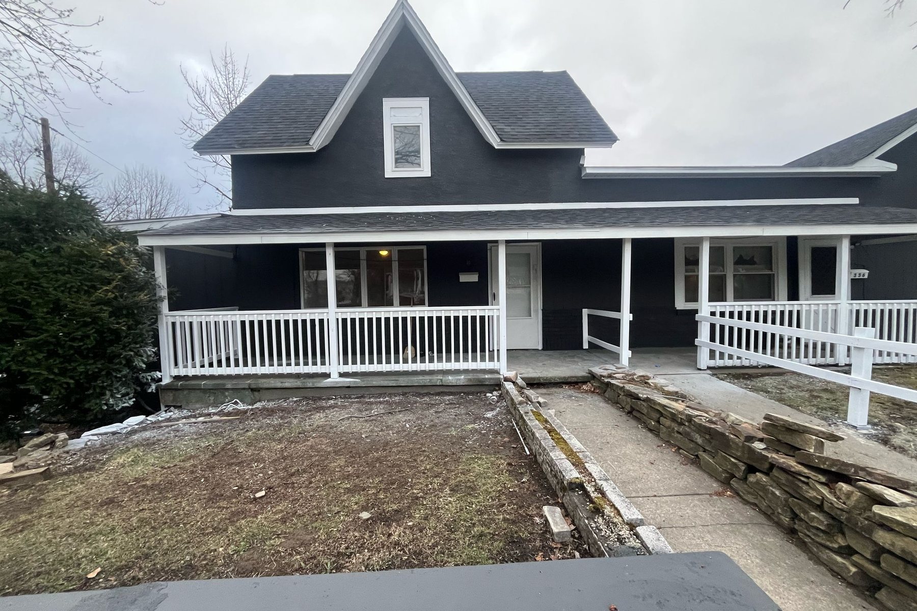 340 N Main Street, Old Forge, after renovation: a large dark-grey building with a full-width white porch and a rebuilt stone retaining wall.