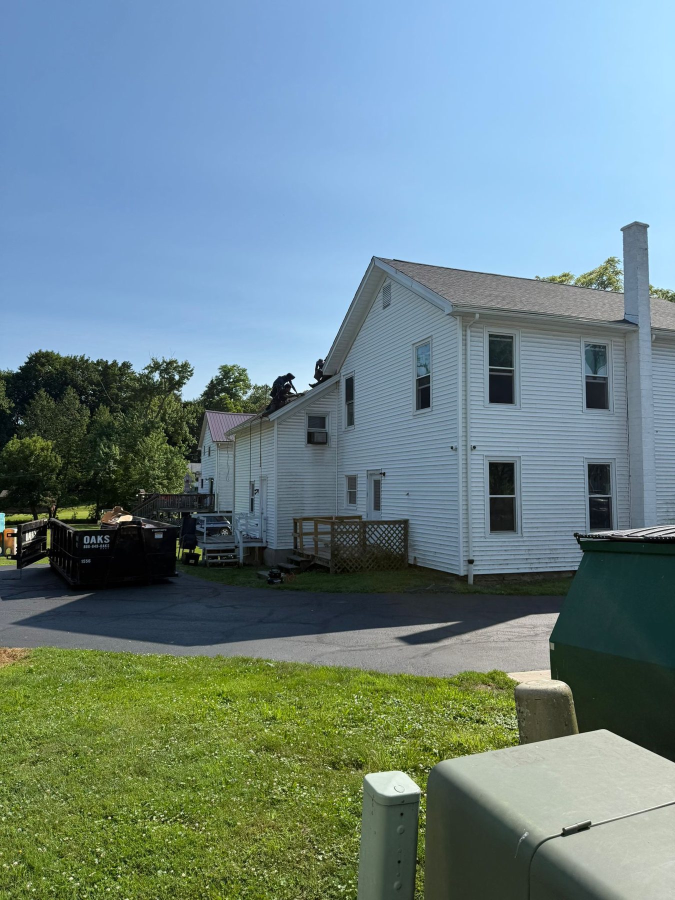 Re-roofing under way at 176 Bridge Street: two roofers on the ridge of the long white building, skips in the yard below and the decks still stripped.
