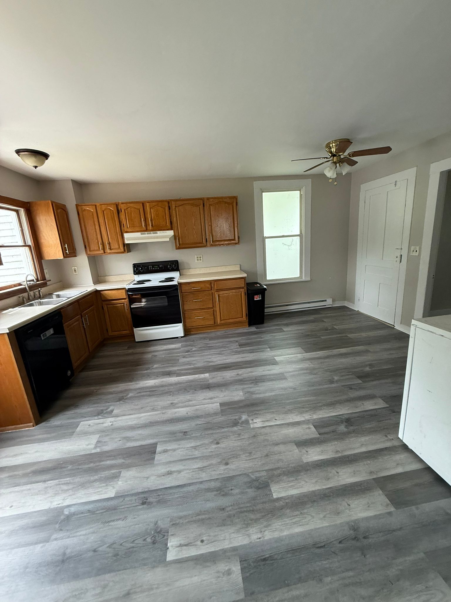 The finished kitchen at 176 Bridge Street: a full run of oak cabinets, a new electric range and dishwasher, and grey wood-look flooring carried through from the next room.