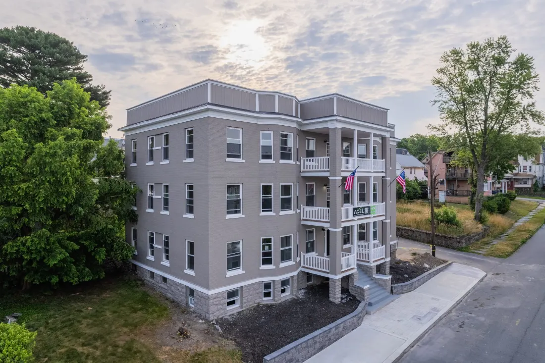 The renovated 12-unit apartment building on Vine Street, Scranton, seen from the air at its corner: three storeys of grey brick with white trim, stacked white porches and a stone base, under an evening sky.