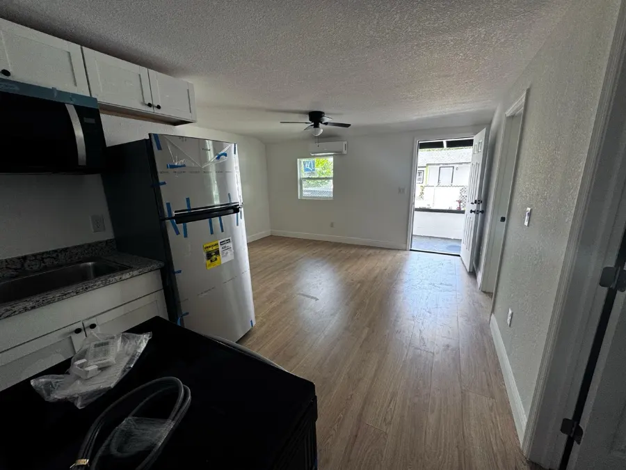 Inside a renovated unit at the Drew Park building: new wood-look flooring, fresh white walls, a wall-mounted air handler and a new refrigerator still in its protective film.