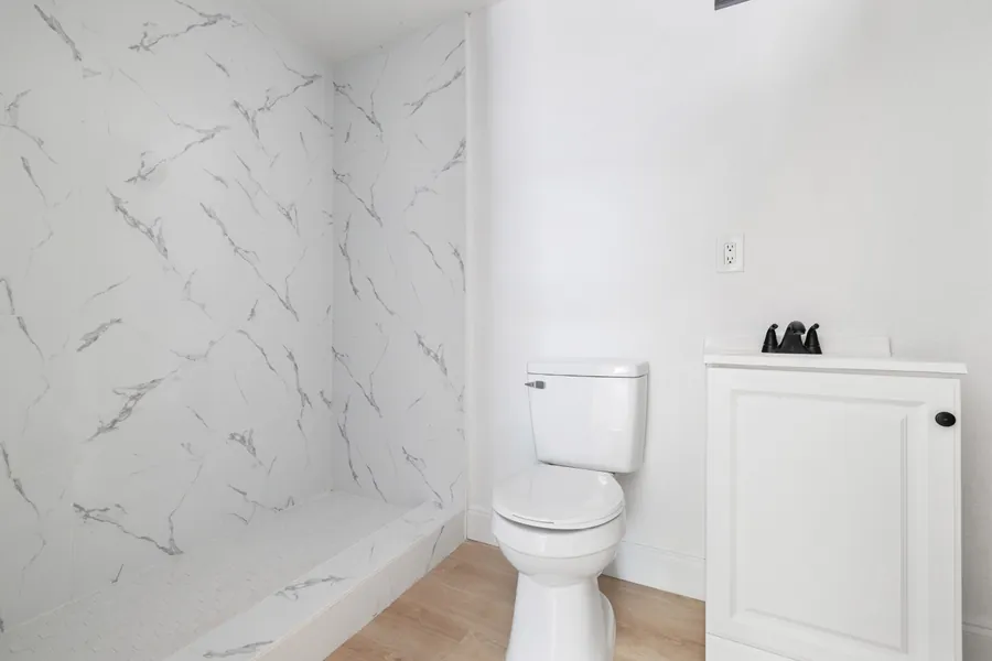 A renovated bathroom at Drew Park: walk-in shower with large marble-look tiles, a new toilet and a white vanity with black fixtures.