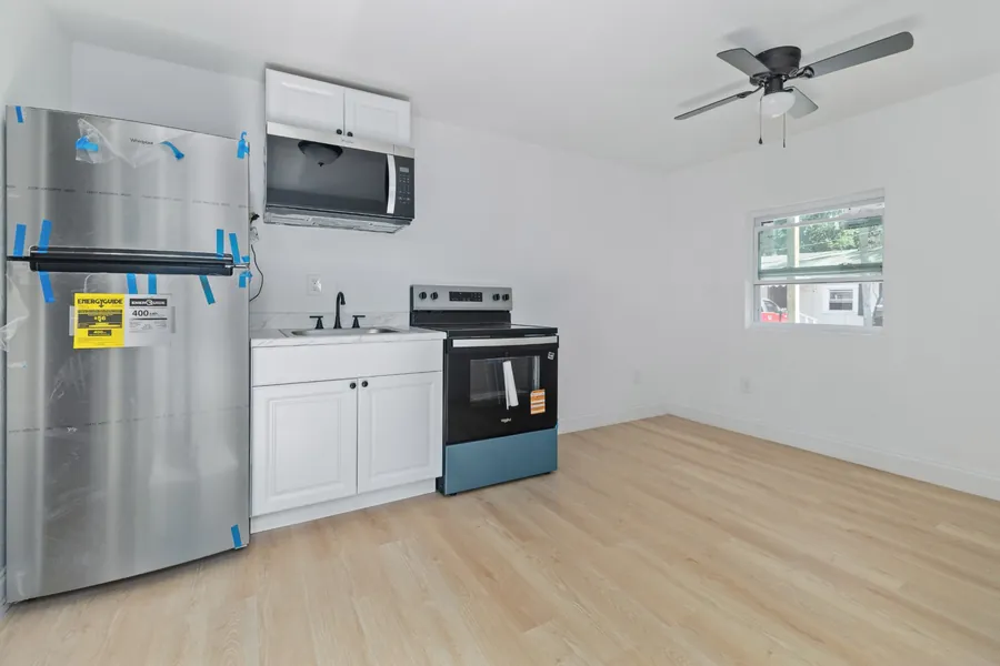 A renovated unit at Drew Park: new kitchen with white cabinets, a stainless refrigerator still in its protective film, a range, and light wood-look flooring.