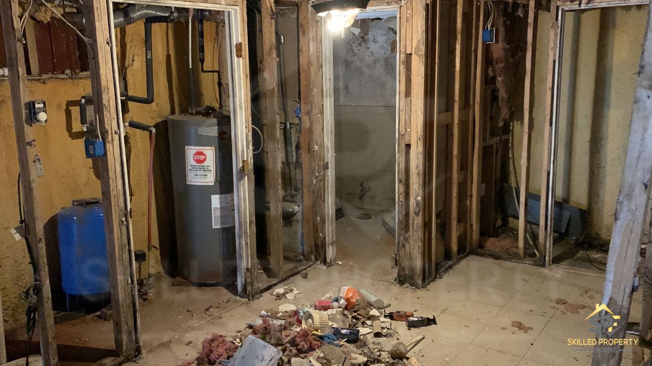 A Northeast Pennsylvania basement as we found it: walls opened to the studs, water heater and pressure tank exposed, demolition debris across the floor.